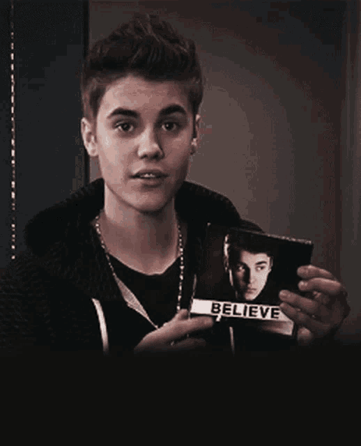 a young man holds up a picture of justin bieber with the words believe on it