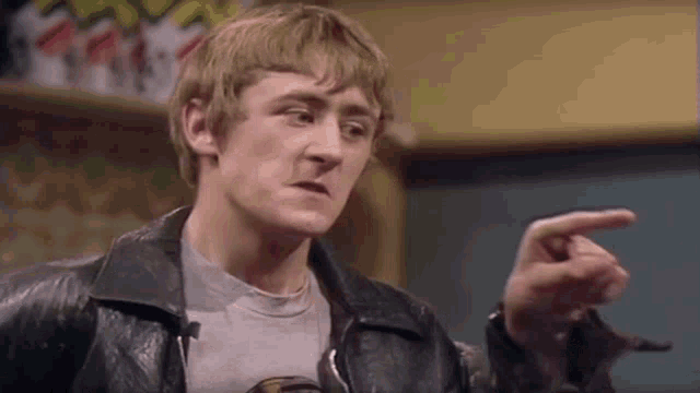 a man in a leather jacket is pointing at something while wearing a gray shirt .