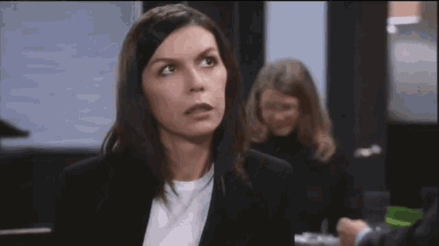 a woman in a black suit and white shirt is looking at the camera
