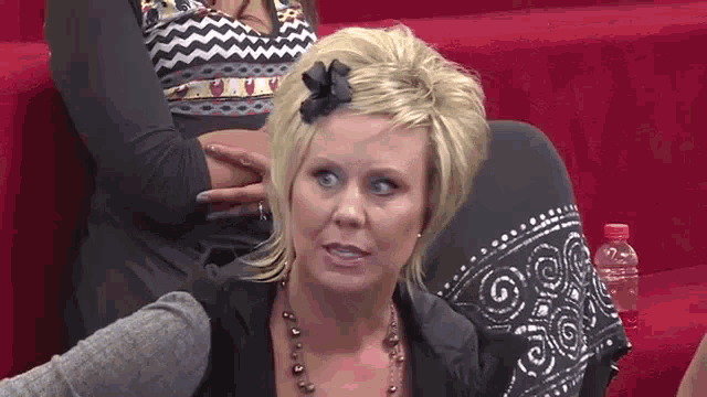a woman with a bow in her hair is sitting on a red couch talking to another woman .