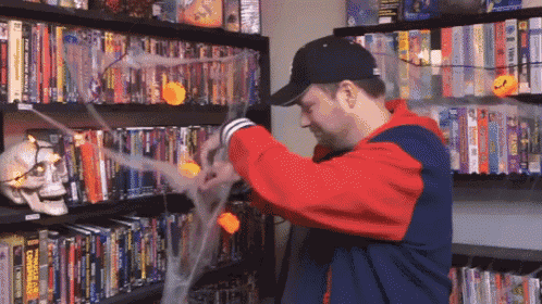 a man in a baseball cap is standing in front of a bookshelf with a skull on it