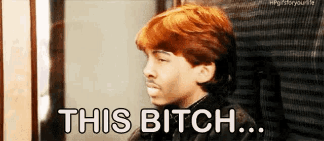 a young man with red hair is sitting in a chair with the words `` this bitch '' written on his face .