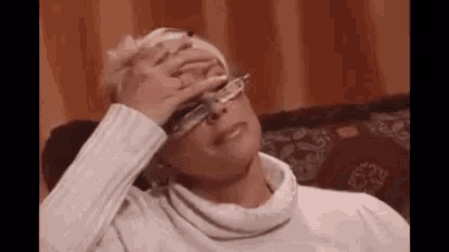 a woman wearing glasses is sitting on a couch and rubbing her forehead .