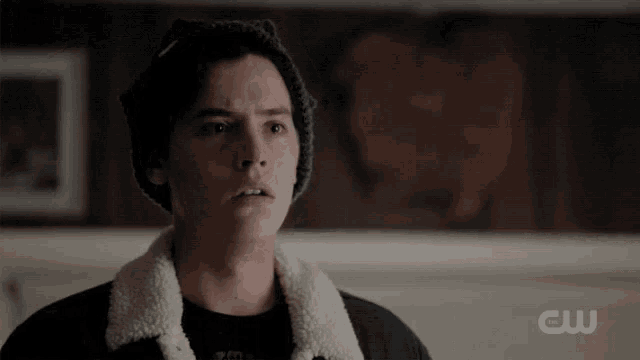 a young man wearing a hat and a sherpa jacket is standing in a room .