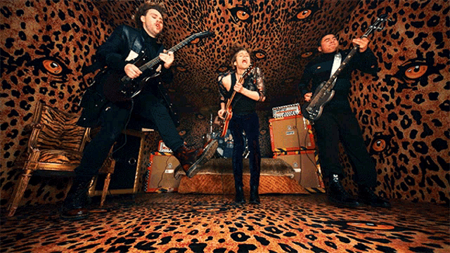 three people playing guitars in a room with a leopard print wall