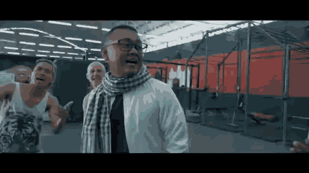 a man wearing glasses and a scarf stands in a gym