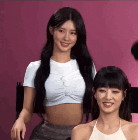 two women are sitting next to each other in front of a pink background .