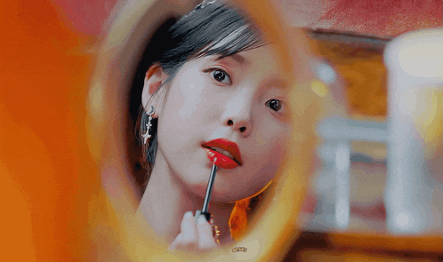 a woman is applying red lipstick in front of a mirror .