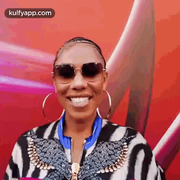 a woman wearing a zebra print jacket and sunglasses is smiling .