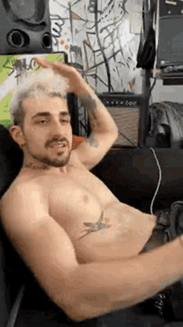 a shirtless man with a tattoo on his chest is sitting on a couch in a room .