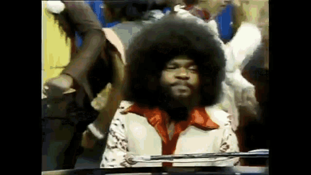 a man with an afro is playing a piano in a crowd .