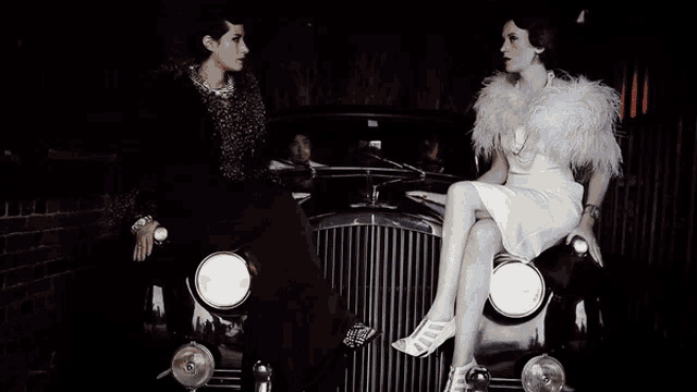 two women are sitting on the front of an old fashioned car