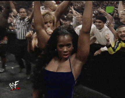 a woman in a blue dress stands in front of a crowd with her arms in the air and the word wwe on the bottom right