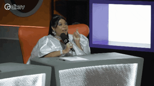a woman sitting at a table with a microphone in front of a screen that says ' aditv ' on it