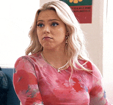 a woman wearing a pink shirt and a necklace with the letter r on it is making a funny face .