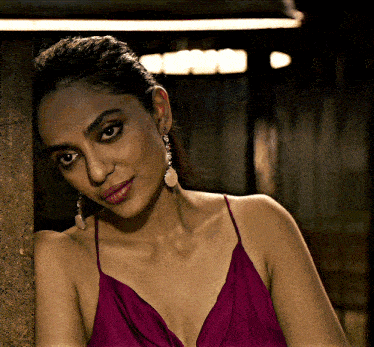 a woman leaning against a wall wearing a purple dress and earrings