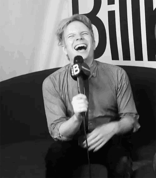 a man is laughing while holding a microphone with a b on it