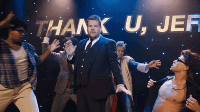 a man in a suit and tie is standing in front of a thank u jeff sign