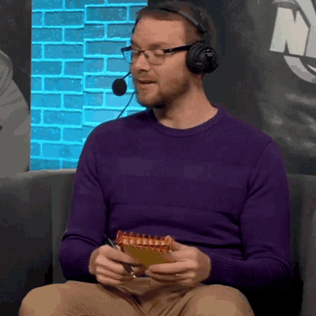 a man wearing a purple sweater and headphones is holding a notebook