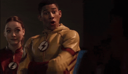 a man and a woman are standing next to each other in a dark room . the man is wearing a flash suit .