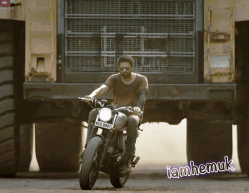 a man is riding a motorcycle in front of a large truck with iamhemuk written in the corner