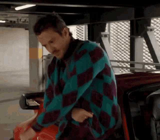 a man in a blue and purple plaid shirt is standing next to a red car