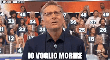 a man in a suit and glasses is standing in front of a crowd and says " io voglio morire "