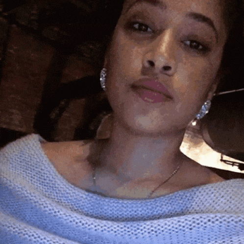 a woman wearing a blue sweater and silver earrings is taking a selfie
