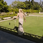 a woman in a white dress is standing on a ledge overlooking a field .