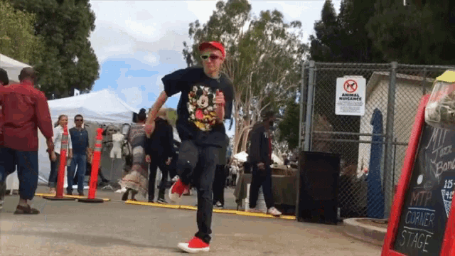 a man wearing a mickey mouse shirt is dancing in front of a no animal nuisance sign