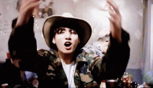 a man wearing a cowboy hat and a camouflage jacket is holding his arms up in the air .