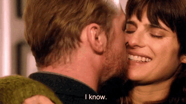 a man is kissing a woman on the cheek and the woman is smiling and says i know