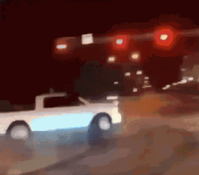 a white truck is driving down a street at night under a red light