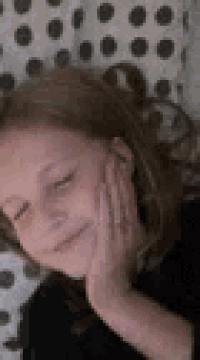 a young girl is laying on a bed with her hand on her face and smiling .