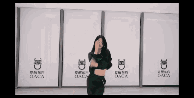 a woman is dancing in front of a wall with oaca on it