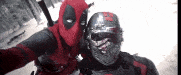 a man in a deadpool costume is taking a selfie next to another man in a helmet .