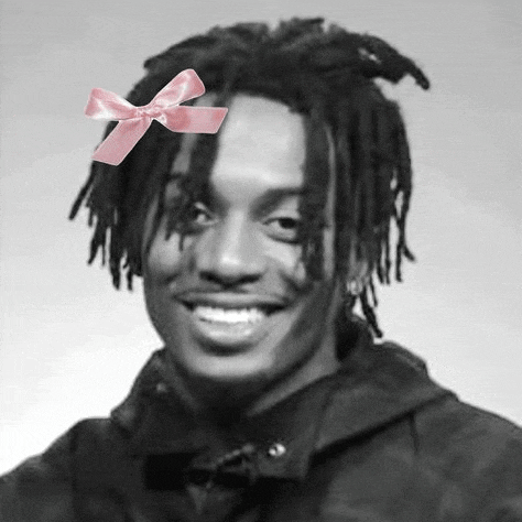 a black and white photo of a young man with dreadlocks wearing a pink bow on his head .