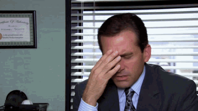 a man in a suit and tie is covering his face with his hand