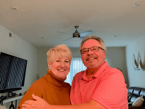 a man and woman posing for a picture in a living room with a ceiling fan in the background