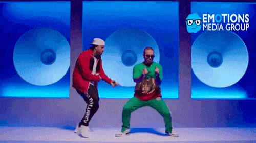 two men are dancing in front of a sign that says " emotions media group "