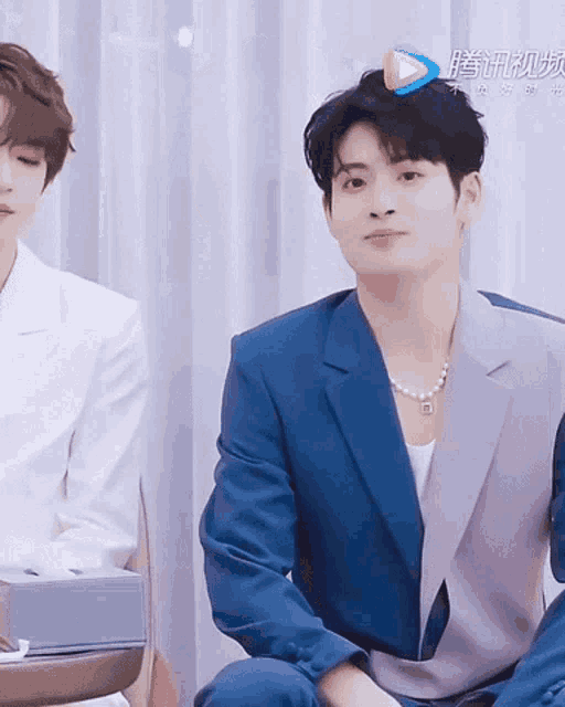 a man in a blue suit sits next to another man in a white suit