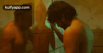 a man without a shirt is standing in front of a mirror .
