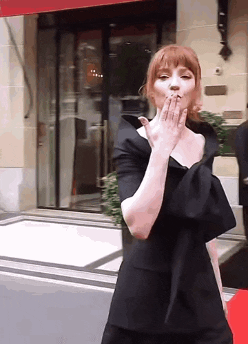 a woman in a black dress is blowing a kiss in front of a building .
