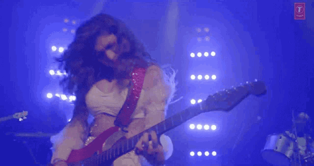 a woman is playing a guitar on a stage with a t on the bottom