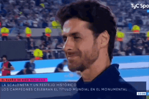 a man with a beard is smiling in front of a crowd on a tv screen