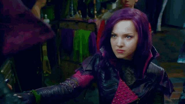 a woman with purple hair and green eyes is wearing a purple jacket and making a funny face .