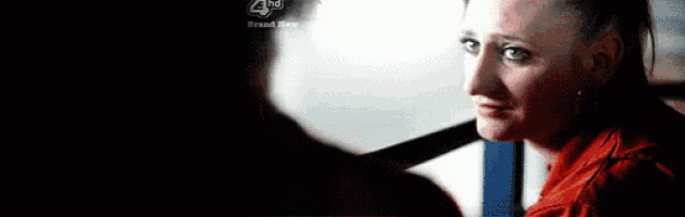 a woman in a red jacket is looking at another woman in a dark room with a 4th brand new logo in the corner .
