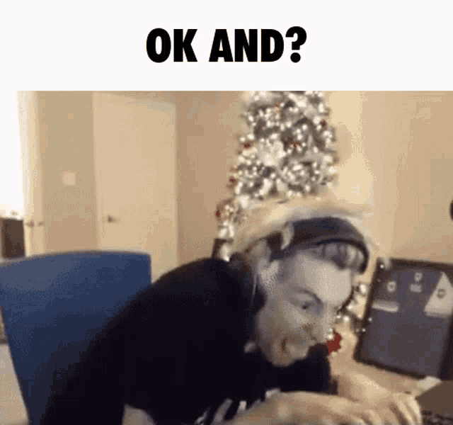 a man is sitting at a desk with a christmas tree in the background and the words ok and ? above him