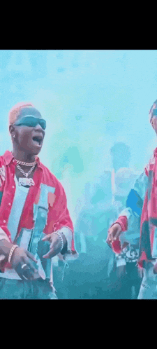 two men are standing next to each other in front of a crowd . one of the men is wearing sunglasses .