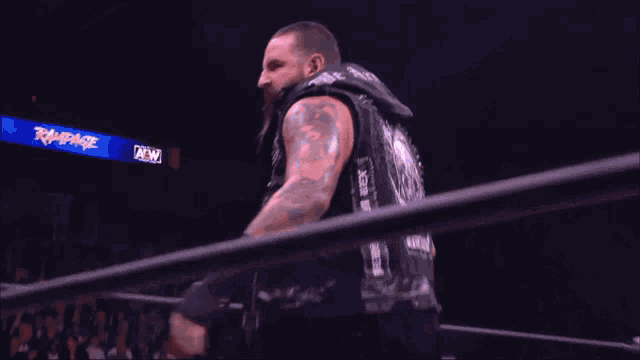 a man with a beard and a tattoo on his arm stands in front of a sign that says rampage